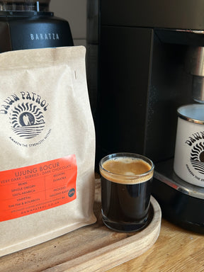 Ujung Bocur Espresso shot in a glass next to a coffee bag and machine on a wooden surface