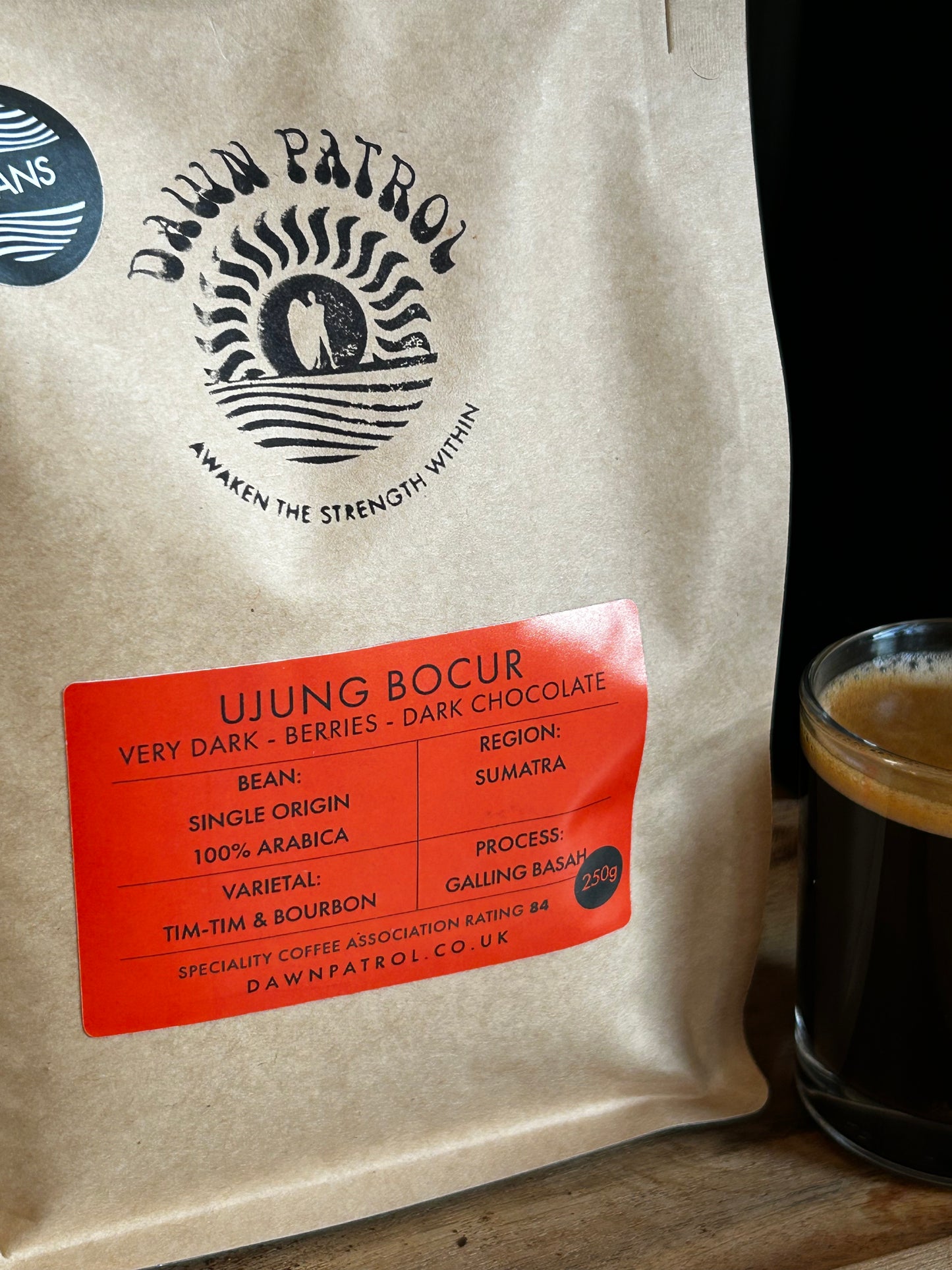 Coffee bag with 'Dawn Patrol' branding and a glass of coffee on a wooden surface