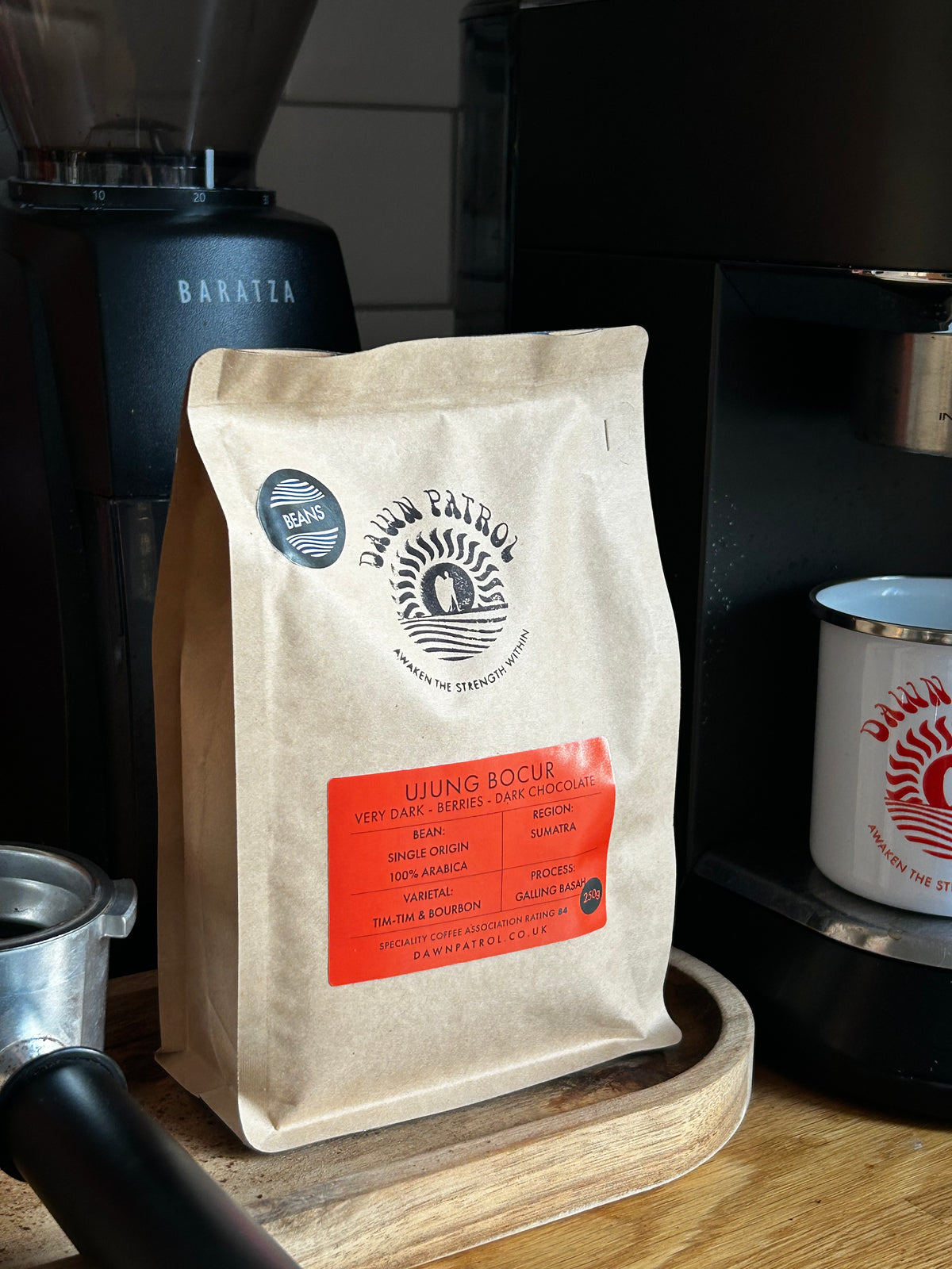 Coffee bag with a visible Dawn Patrol brand logo on a wooden surface with coffee-making equipment in the background.